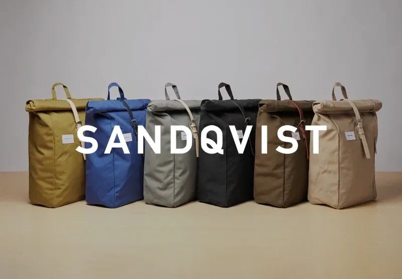 Six Sandqvist rolltop backpacks in a row in different colours, the Sandqvist wordmark across them